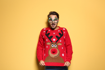 110695326 - young man in christmas sweater with party glasses on color background