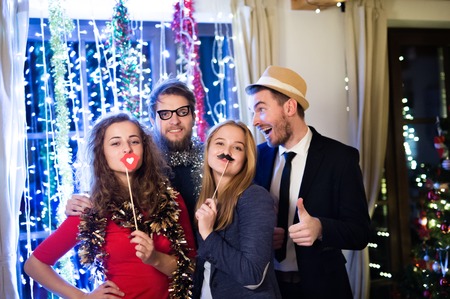 67160956 - beautiful hipster friends with photobooth props celebrating the end of the year, having party on new years eve, chain of lights behind them.