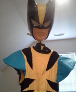 A mannequin wears a superhero costume with a black helmet and yellow and blue suit, resembling a comic book character.