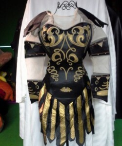 Black and gold medieval-inspired costume with intricate patterns displayed on a mannequin against a green backdrop.