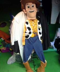A life-sized character costume of a cowboy figure with a brown hat, yellow shirt, and blue pants, leaning against a rack.