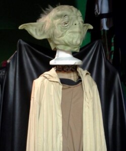 A Yoda mannequin dressed in a beige robe against a dark backdrop.